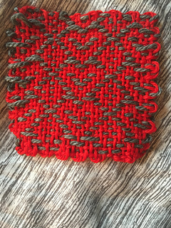 A red woven coaster, featuring gray outlined hearts and diamond motifs on it, back view