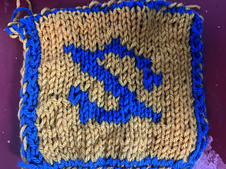 A double-knitted blanket square. This is the back of the square, featuring a styled blue reversed 'Z' on a field of gold.