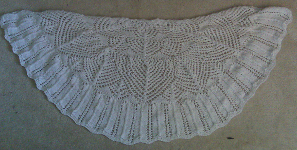 A lacy half-circle knitted shawl in white, featuring cascading arched designs on the body with a feather border.