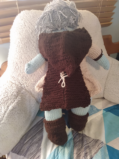 A knitted doll, back view. You can clearly see the hooded cape she is wearing.